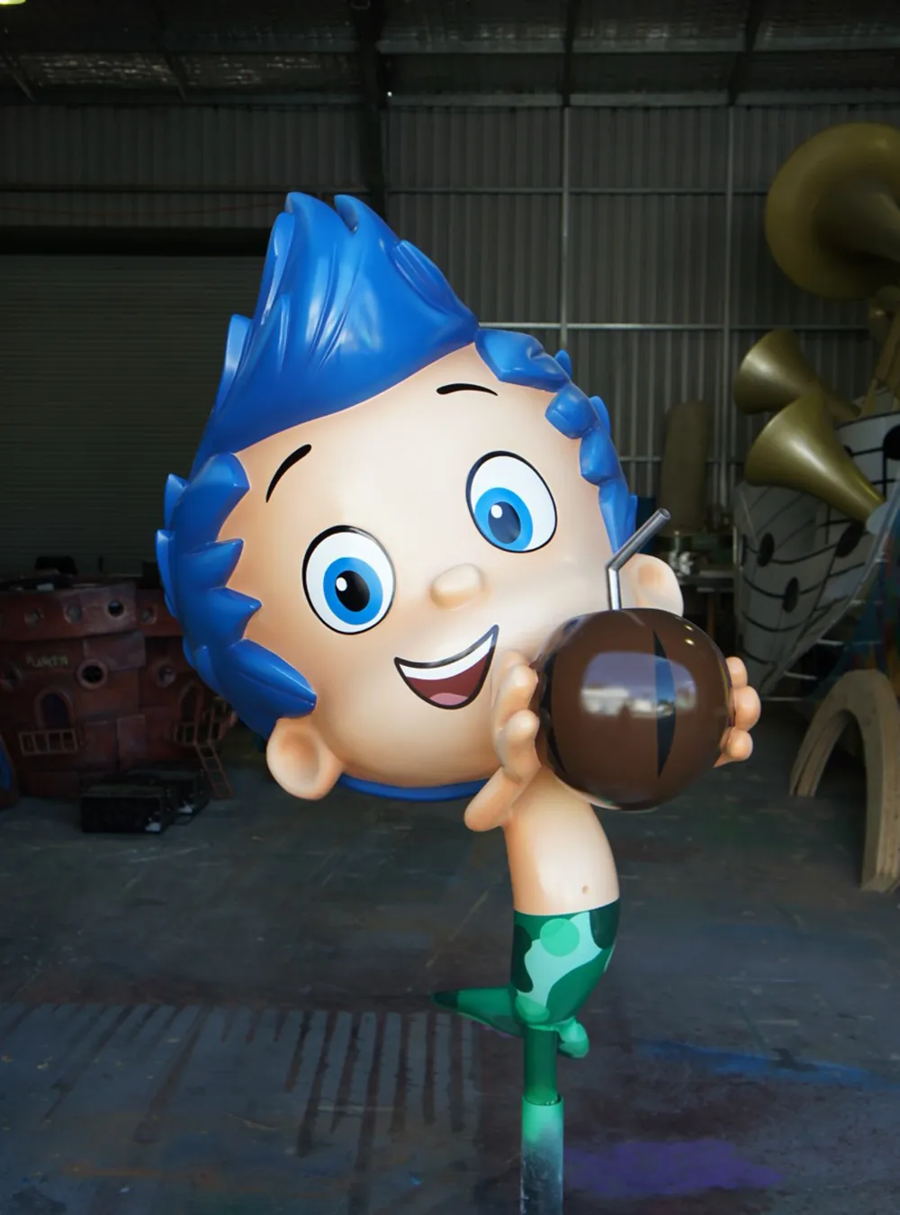 Bright and playful sculpture of a young boy character with blue hair, excitedly holding a coconut drink, set against the backdrop of a workshop, created by Sculpt Studios.
