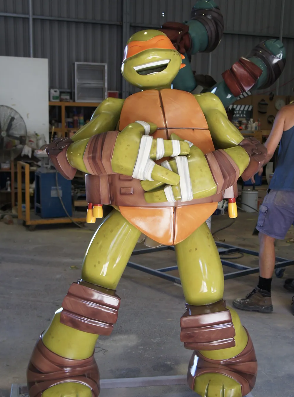 Lifelike sculpture of Michelangelo, the Teenage Mutant Ninja Turtle, confidently holding nunchaku, set in a workshop, designed and created by Sculpt Studios.