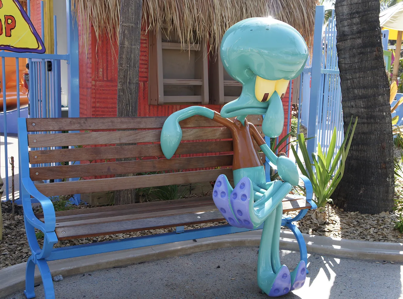 Large turquoise sculpture of Squidward from SpongeBob SquarePants sitting on a park bench.