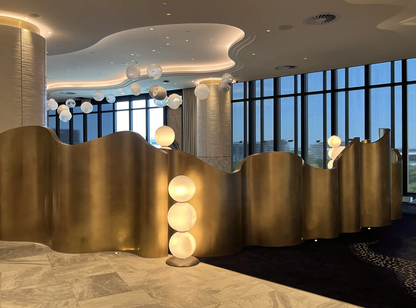 Golden wavy brass partition in Brisbane's Queens Wharf High Roller’s Room, accentuated by glowing overhead globe lights.