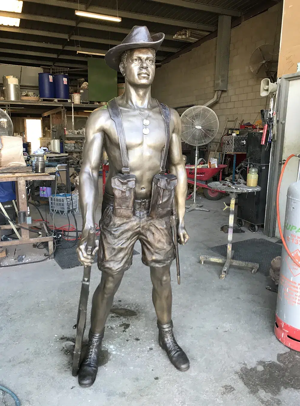 Completed bronze statue of a soldier, crafted by Sculpt Studios, showcased in a workshop with various tools and equipment in the background.